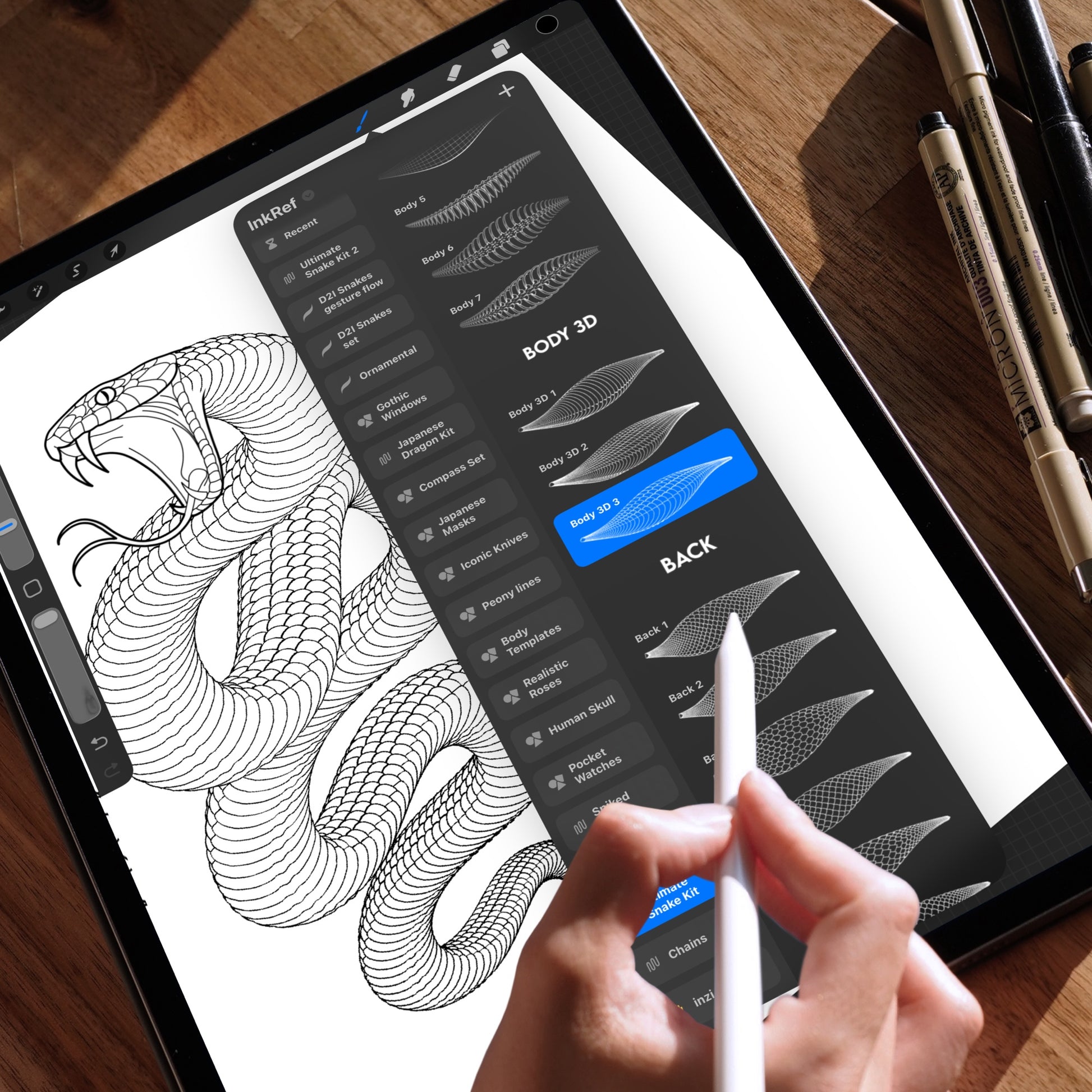 Hand holding an Apple Pencil using the Procreate app on an iPad, displaying a snake drawing created with Procreate brushes. The brush selection panel is open, highlighting the “Snake Body” and “Body 3D” brushes used to build detailed snake scale patterns. The iPad is placed on a wooden table with technical pens in the background.